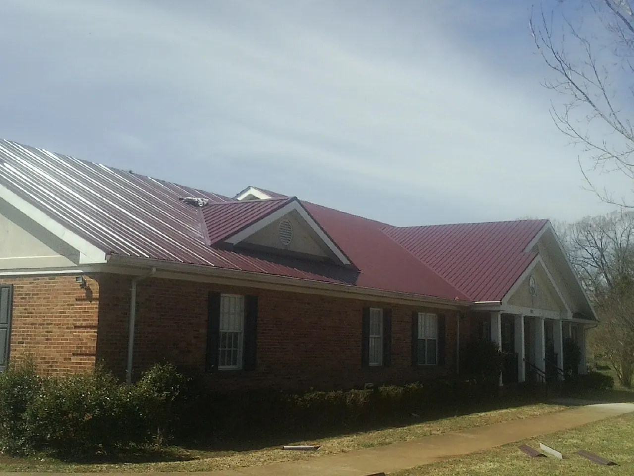 Red metal roof with gabled entries on a long brick building, from a Hail Damage Roof Repair job in Souderton