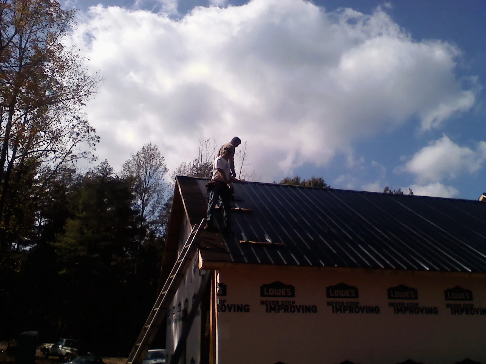 Roofer fastening dark metal panels high against a cloudy sky, from a Roof Inspection job in Souderton