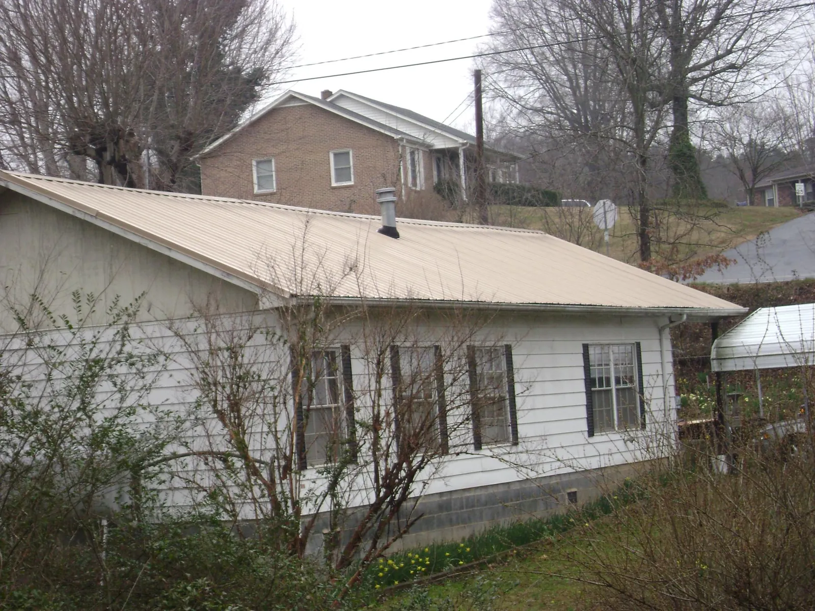 Tan metal roof on a white sided house set into a hillside — Commercial Roofing by Roofing Brothers in Souderton